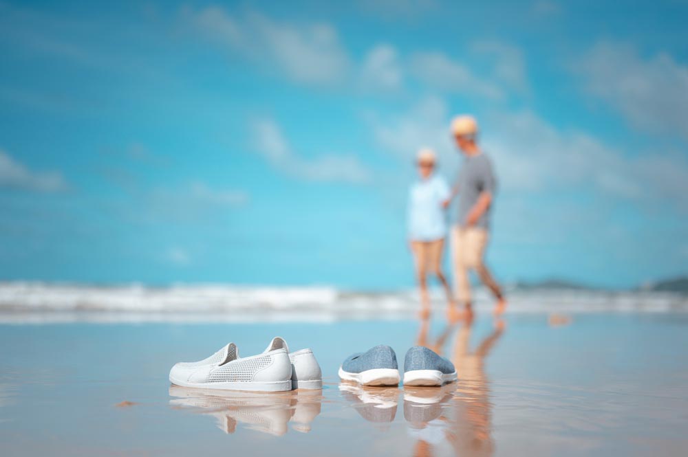Couple enjoying retirement abroad walking along beach with shoes in foreground