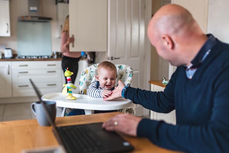 Father on laptop in kitchen with child and mother